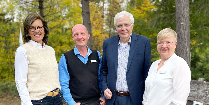 Vier Mitarbeiter des Sporthotel Grafenwald stehen nebeneinander vor grünen Bäumen