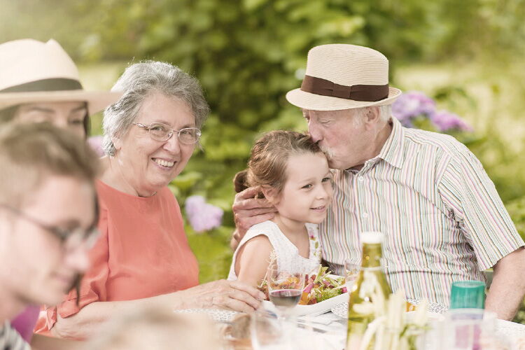 Familie mit Eltern, Kinder und Großeltern sitzen gemeinsam am gedeckten Tisch im Freien