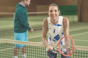 Eine Tennisspielerin im Sportoutfit steht mit Tennisschläger auf dem Tennisplatz am Netz.
