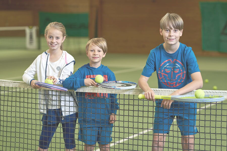 Kids Tennis Kinder stehen auf dem Tennis Spielfeld und lächeln in die Kamera