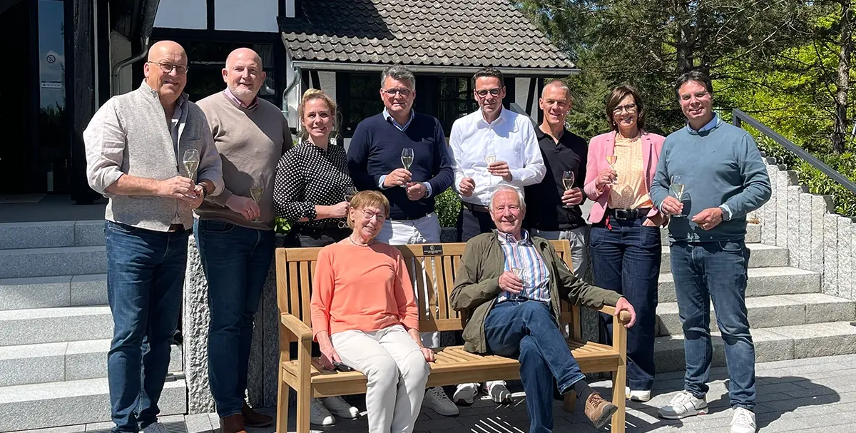 Gruppenbild mit Personen um gespendeter Parkbank vor dem Eingang des Hotels