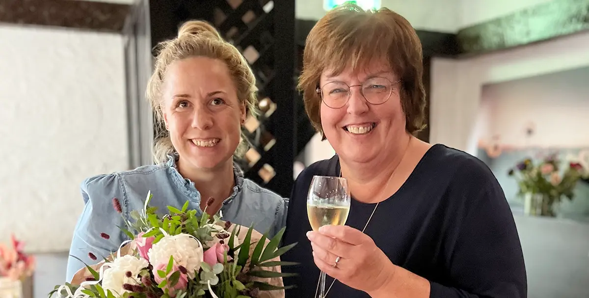 Hoteldirektorin Jennifer Kürsten und Ute Lenarz posieren mit Sektglas und Blumenstrauß