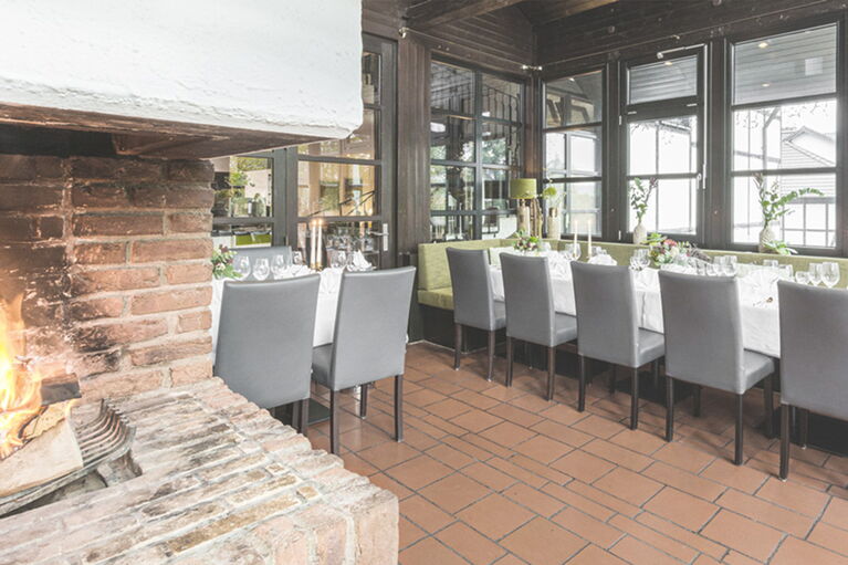Blick ins Kaminzimmer mit schön gedeckten Tischen und gemütlichem Kaminfeuer