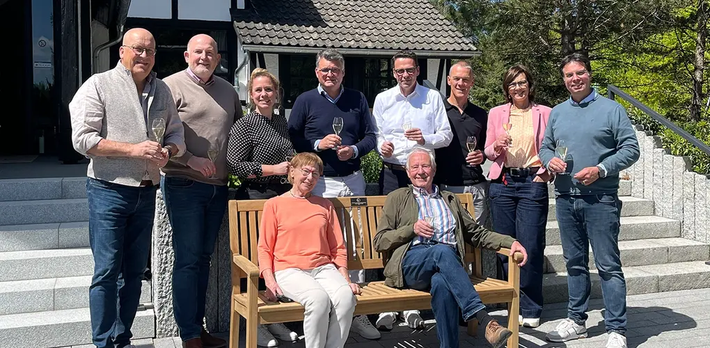 Gruppenbild mit Personen um gespendeter Parkbank vor dem Eingang des Hotels