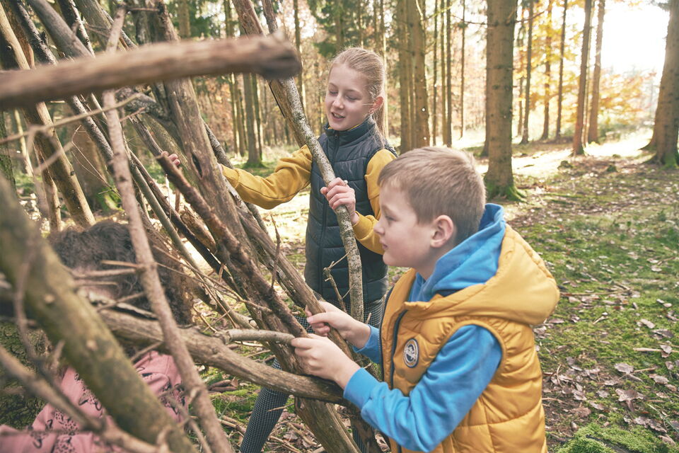 Kids Club Kinder bauen im Wald gemeinsam eine Hütte aus Ästen