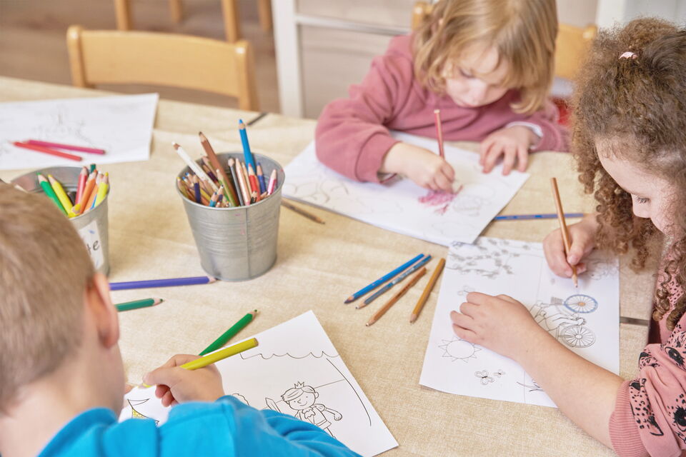 Drei Kinder malen im Kids Club konzentriert Malvorlagen aus