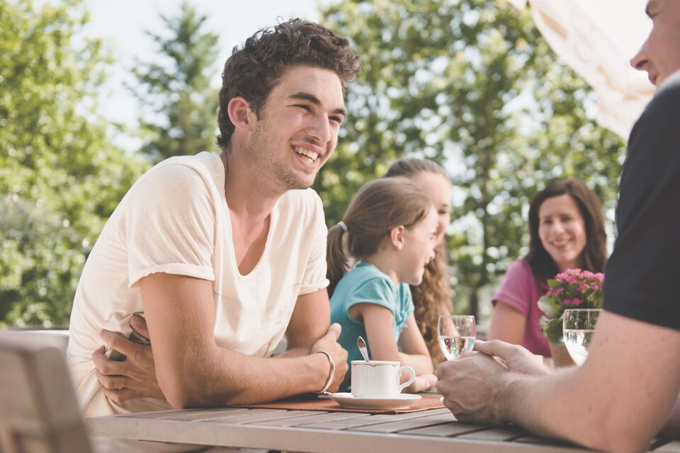 Familie sitzt auf der Sonnenterrasse des Sporthotel Grafenwald und unterhält sich angeregt