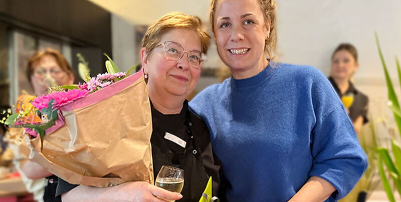 Natalie Maurer hält einen großen Blumenstrauß und ein Glas Wein in den Händen und steht neben Jennifer Kürsten