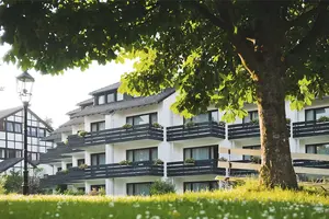 Blick über eine grüne Hecke hinweg auf die Balkone des Apartmenthauses. Im Vordergrund ein grüner Baum.